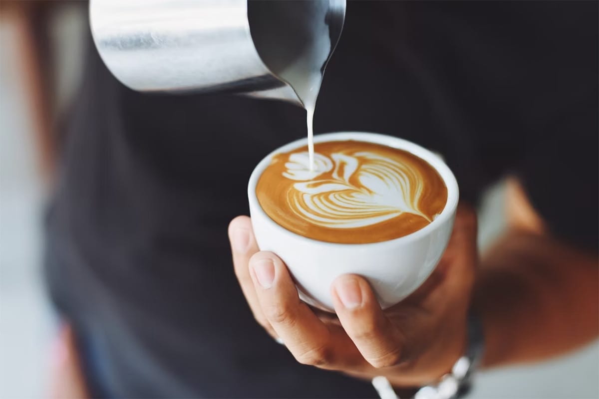 Barista pouring steamed milk into a cup to create latte art.