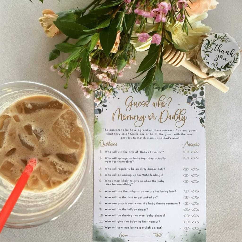 Iced coffee beside a “Mommy or Daddy” baby shower game card and floral arrangement