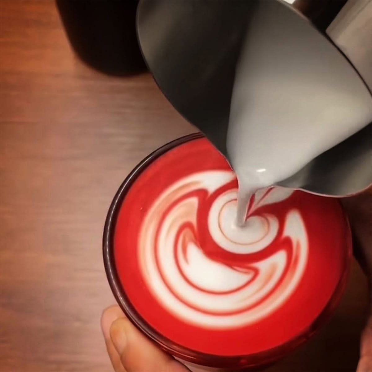 Milk being poured into a red cup to create latte art.