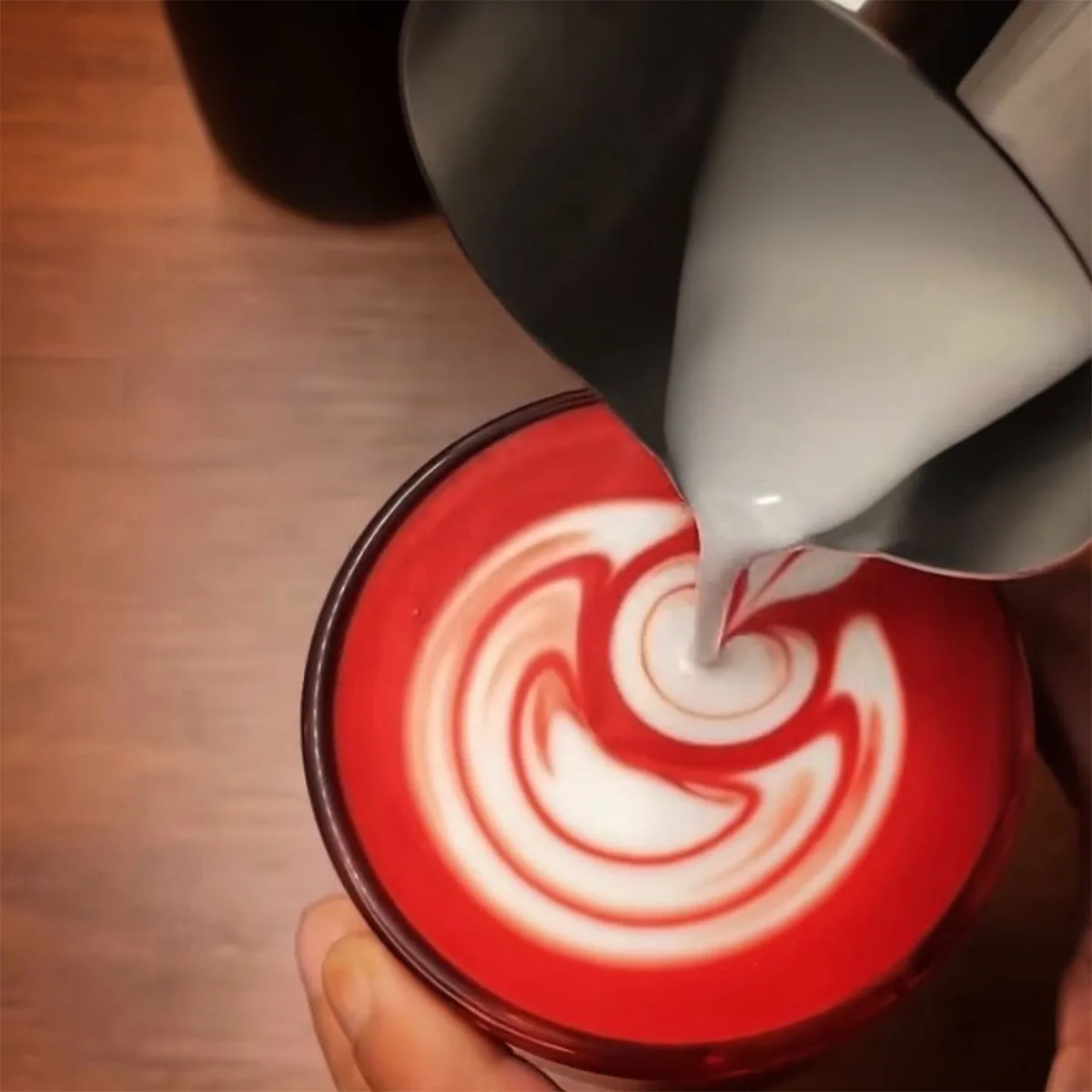 Milk being poured into a red cup to create latte art.