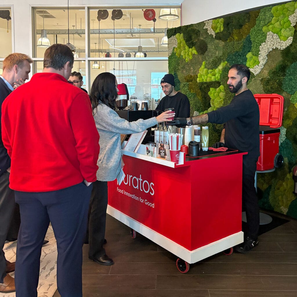 Coffee Malem barista handing a drink to a guest from a branded Puratos coffee cart in Philadelphia in 2026.