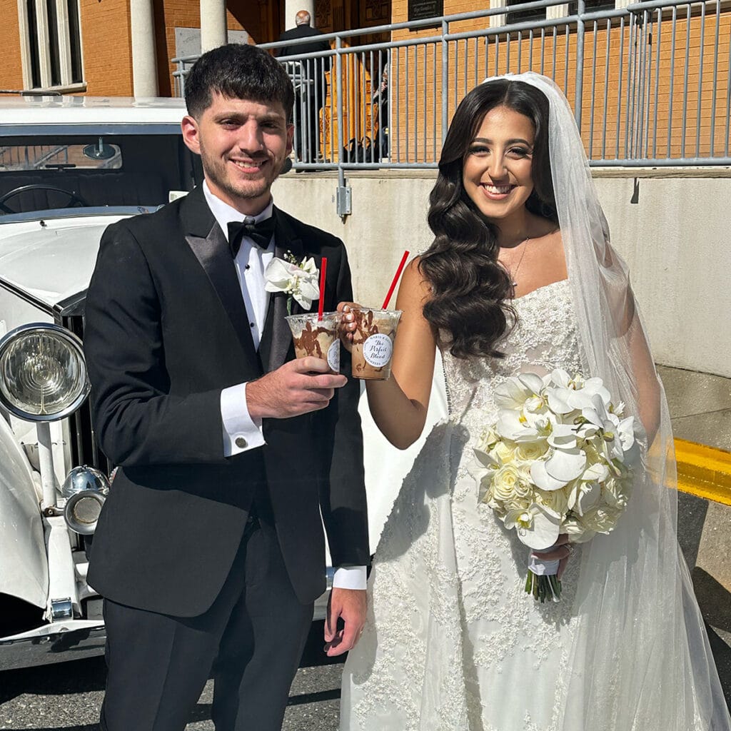 Bride and groom holding Coffee Malem drinks beside a vintage car